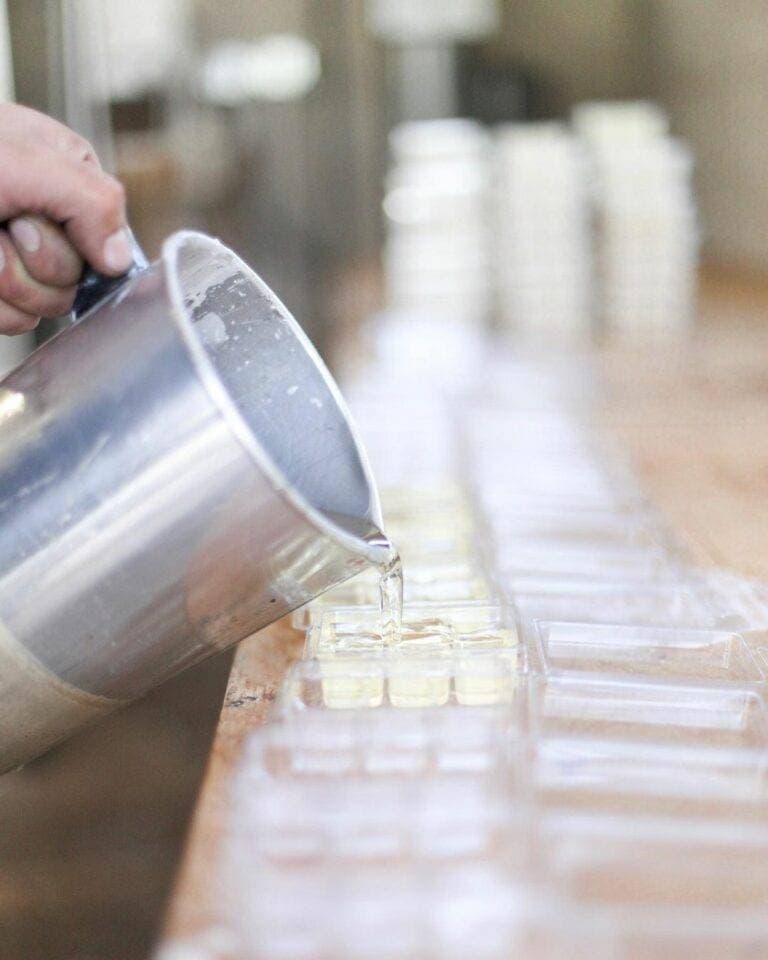 A hand pours melted wax into a row of clear wax melt molds during small-batch production.
