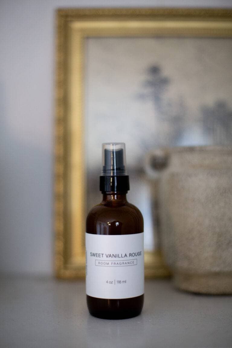 A brown glass bottle labeled "Sweet Vanilla Rouge Room Fragrance" stands on a white surface.