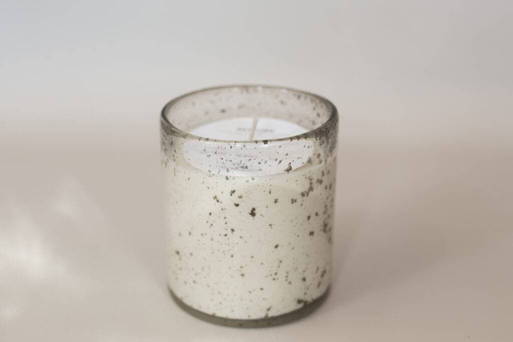 A close-up of a speckled glass jar candle with cream-colored wax.